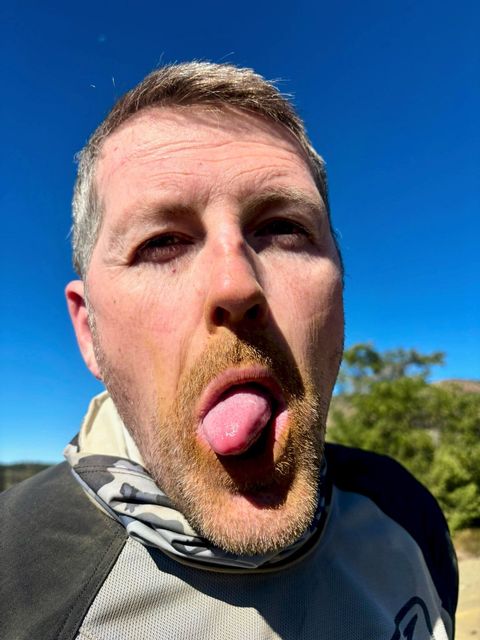 Man sticking out his tongue with a mischievous expression against a blue sky.