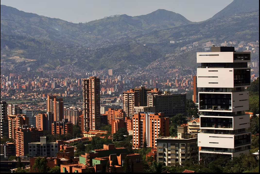 City skyline with mountains in the background. Modern white tower in the foreground, other buildings are mostly brick-colored.