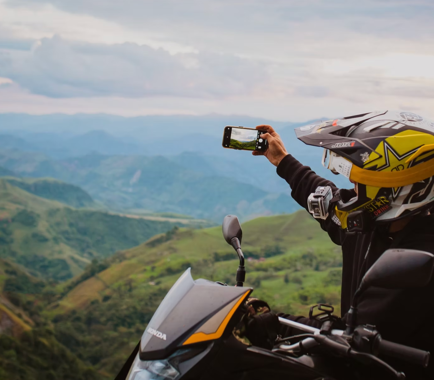 Person on motorcycle, taking photo of mountain range with phone.