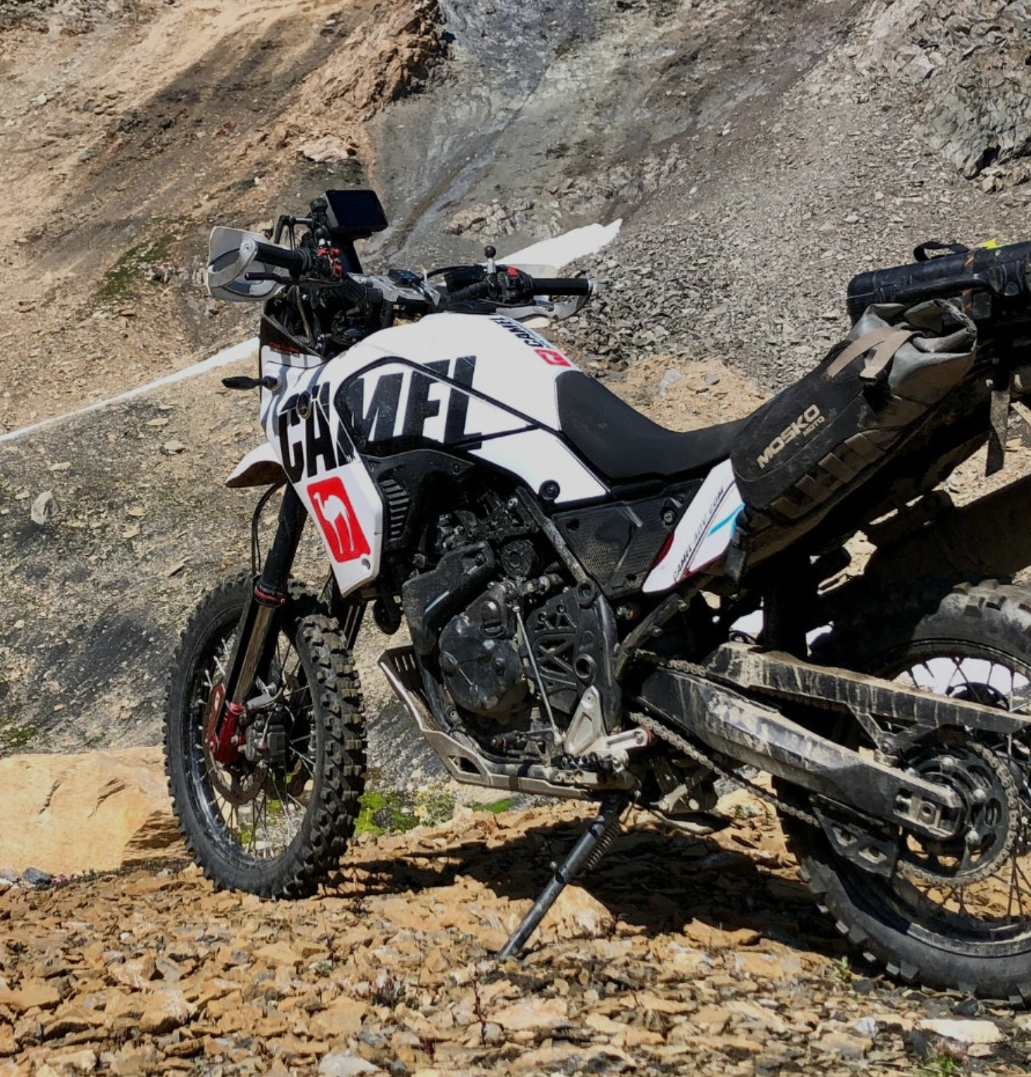 White and black adventure motorcycle on a rocky mountain slope, with bags and protective gear.