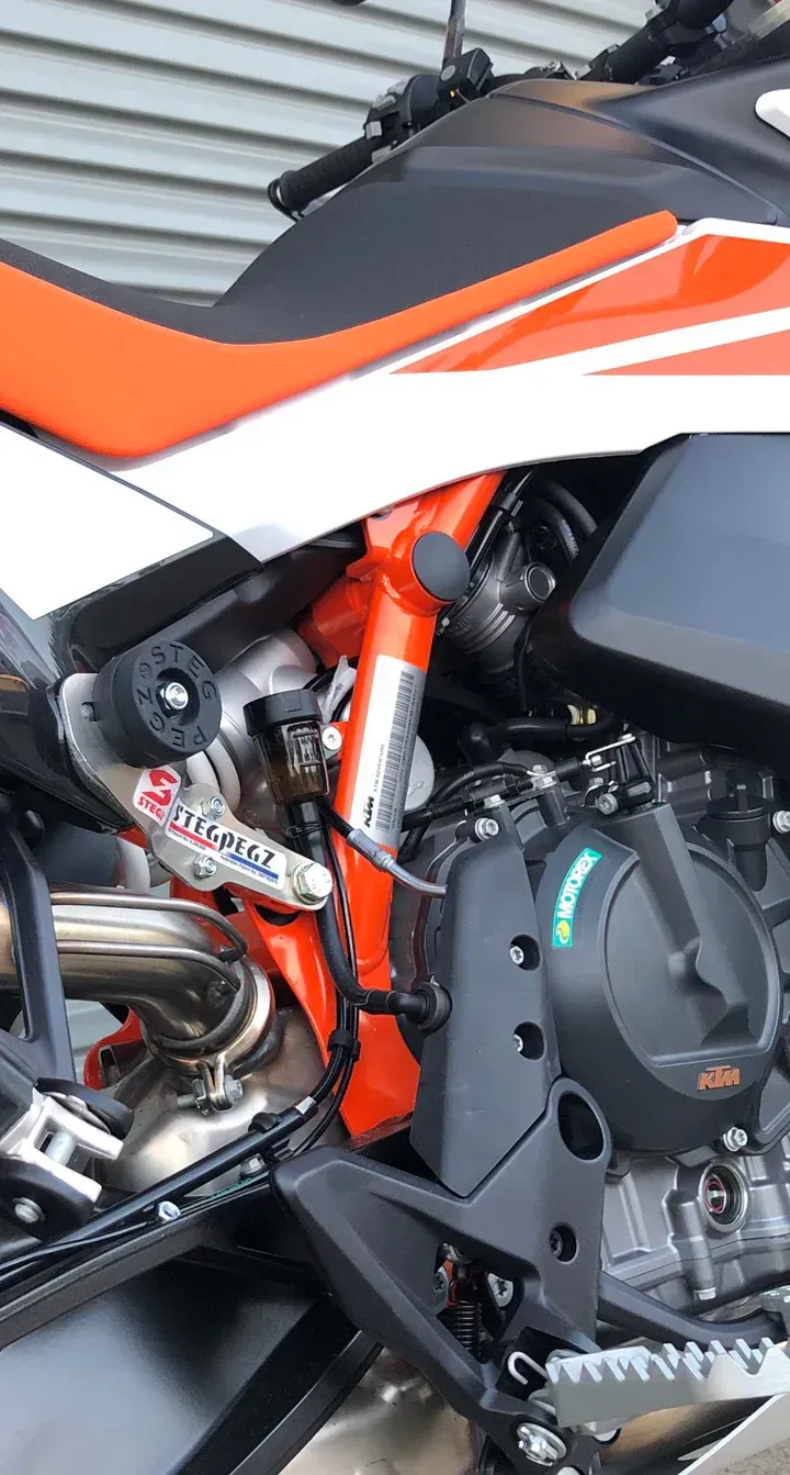 Orange and black KTM motorcycle frame and engine details, showing exhaust, suspension components, and engine case.