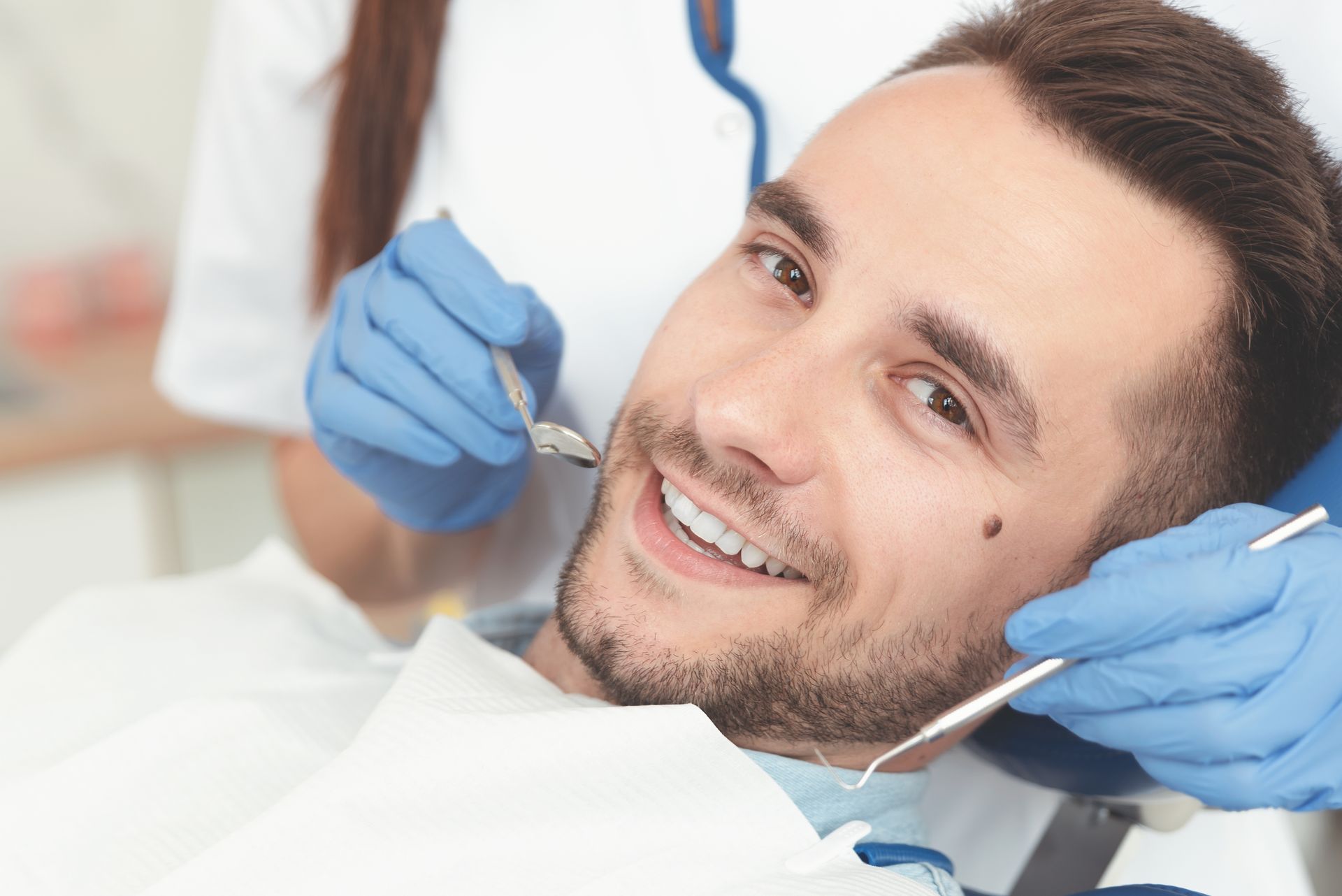 Smiling man in dental chair during exam by gloved dentist.