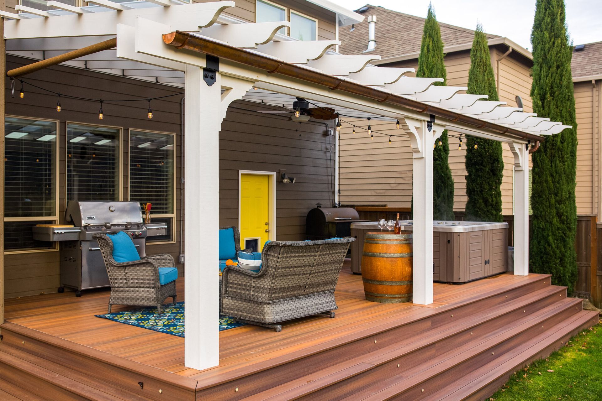A patio with a pergola , chairs , a grill and a hot tub.