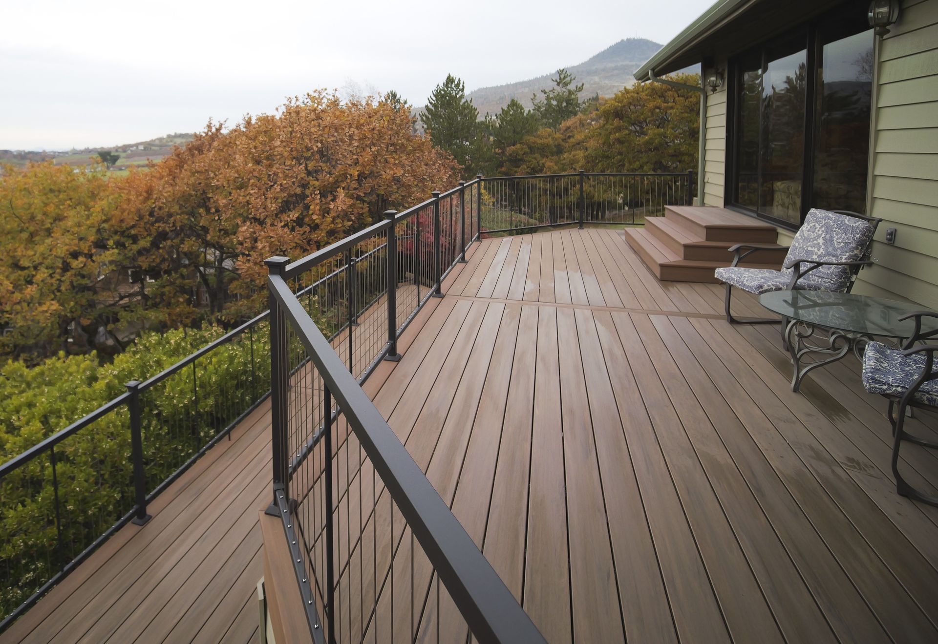 Wooden deck overlooking a scenic landscape. Black railing surrounds the deck. Patio furniture sits on the right.