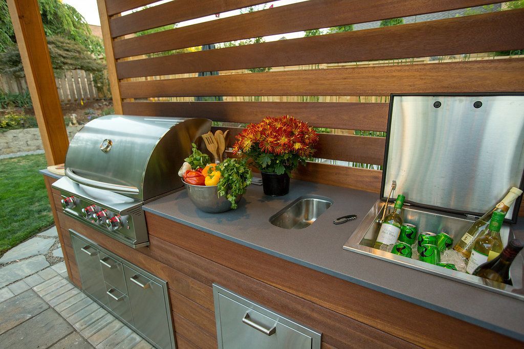 Outdoor kitchen with grill, sink, and cooler; brown wood paneling, gray countertop.