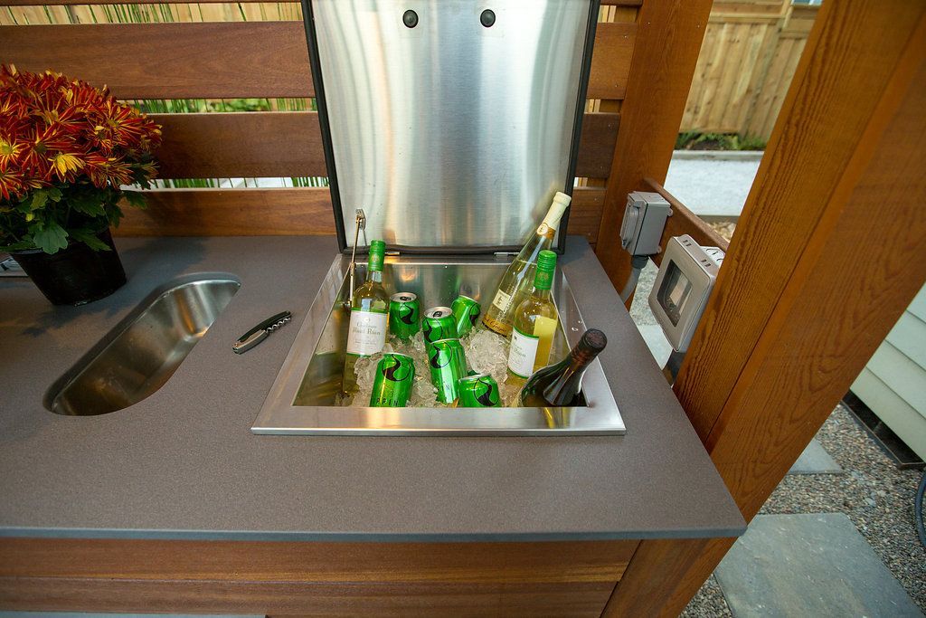 Outdoor kitchen countertop with built-in cooler holding drinks on ice, brown wooden frame.