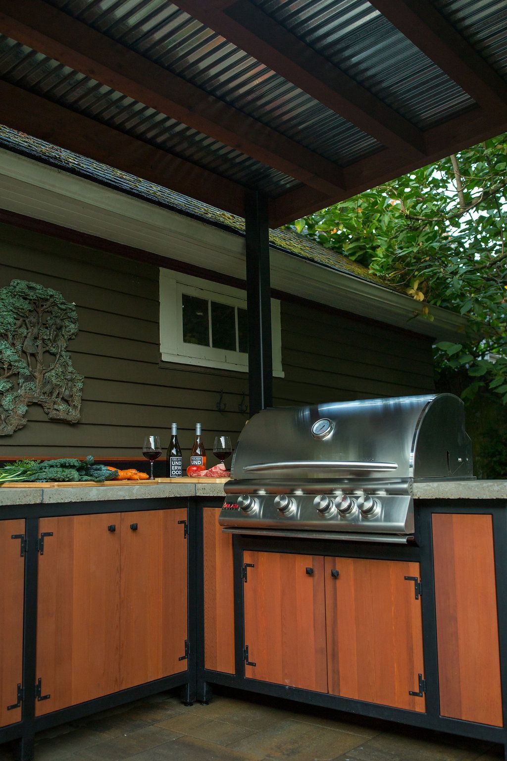 Outdoor kitchen with stainless steel grill, wooden cabinets, and corrugated metal roof.