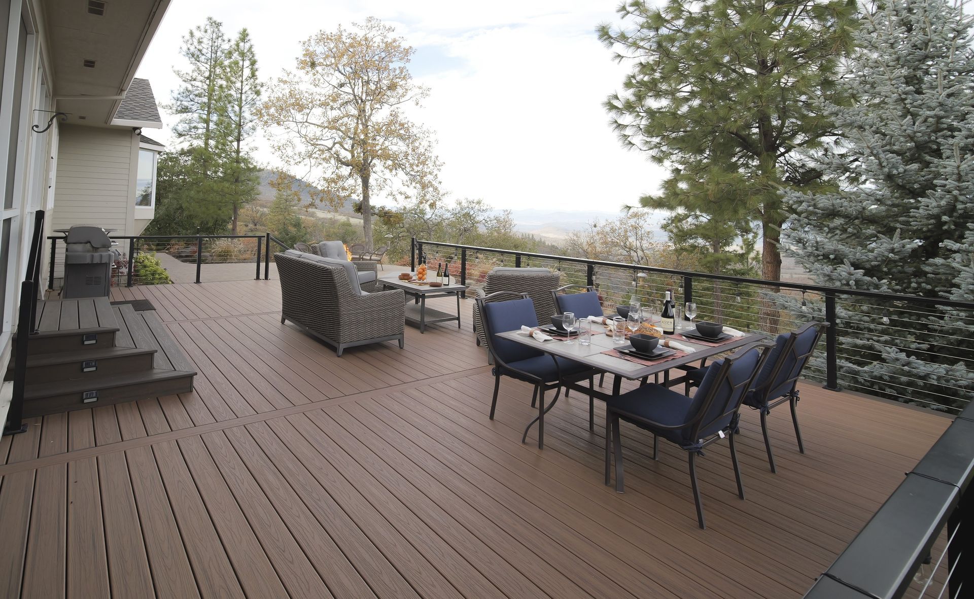 Deck with outdoor furniture overlooking a scenic vista; brown deck, blue chairs, green trees.