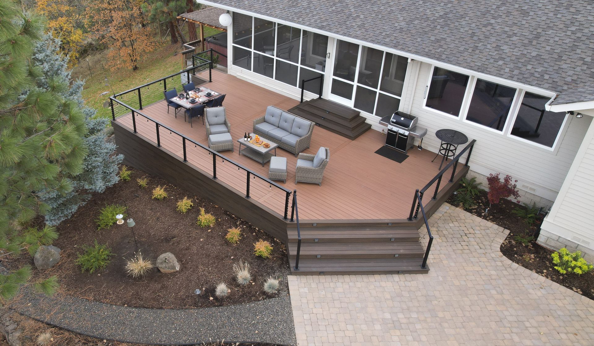 Aerial view of a multi-level deck with outdoor furniture, steps leading down to a brick patio, and a house with screening.