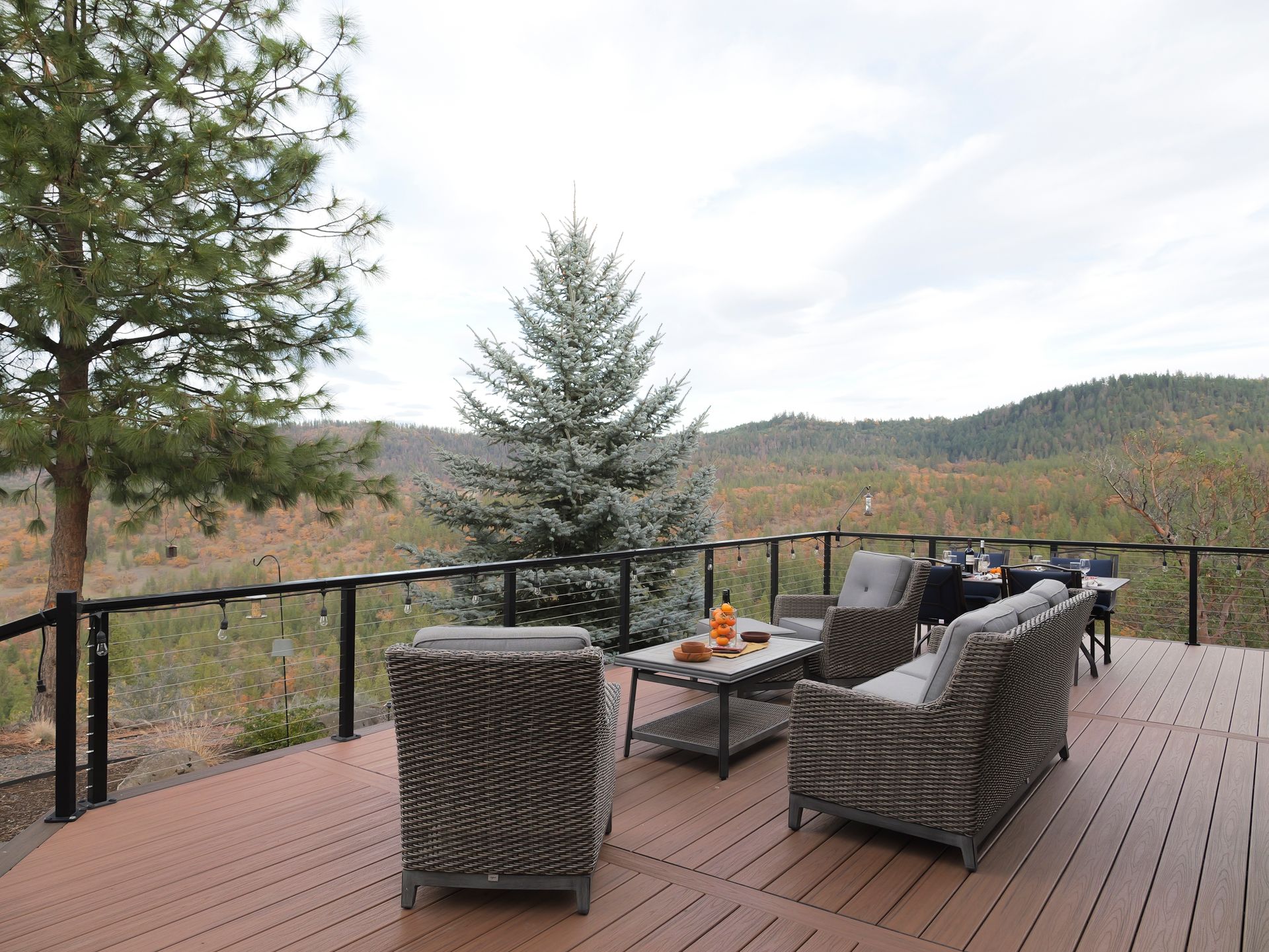 Deck with outdoor seating overlooking a scenic landscape with trees and a cloudy sky.