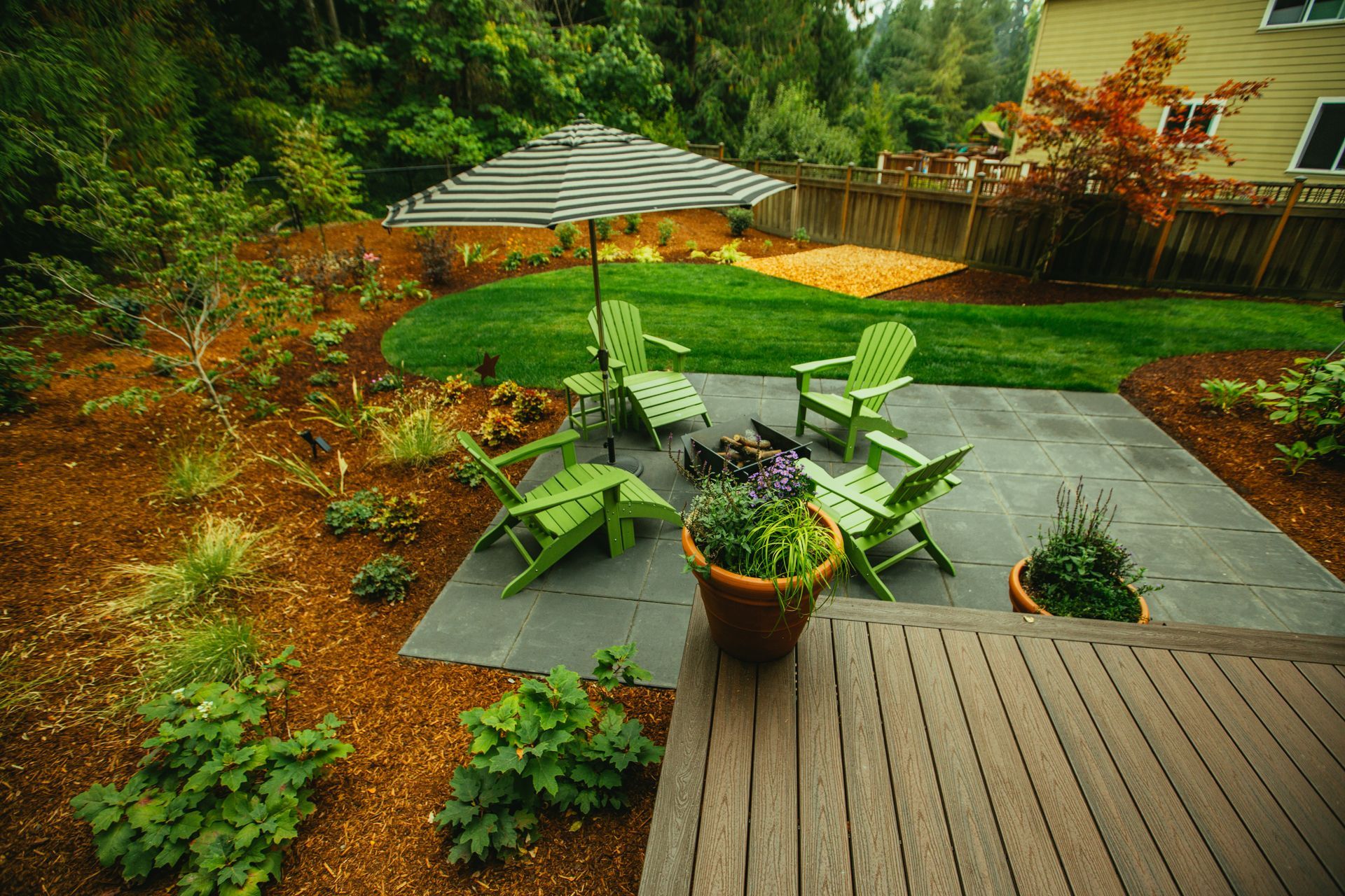 Backyard patio with green Adirondack chairs, umbrella, and fire pit.