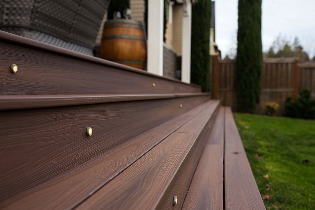 Close-up of brown wooden deck steps with embedded lights, leading to a porch and yard.