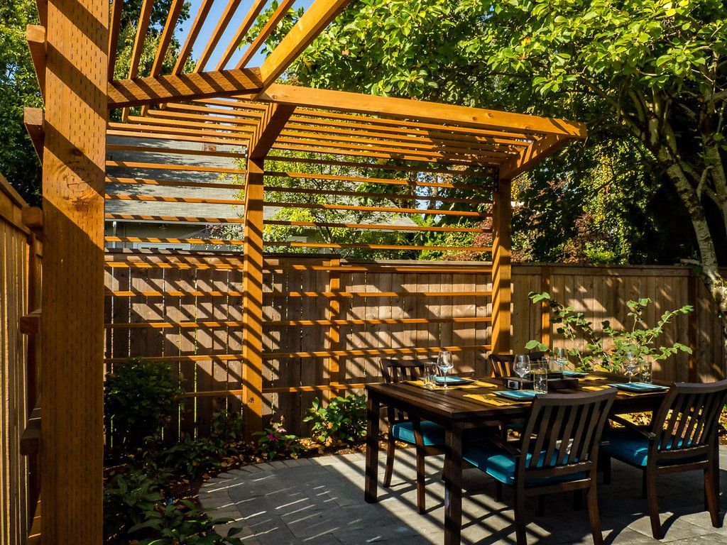 A patio with a table and chairs under a wooden pergola.