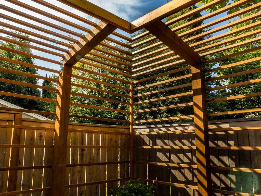 A wooden pergola is sitting next to a wooden fence.