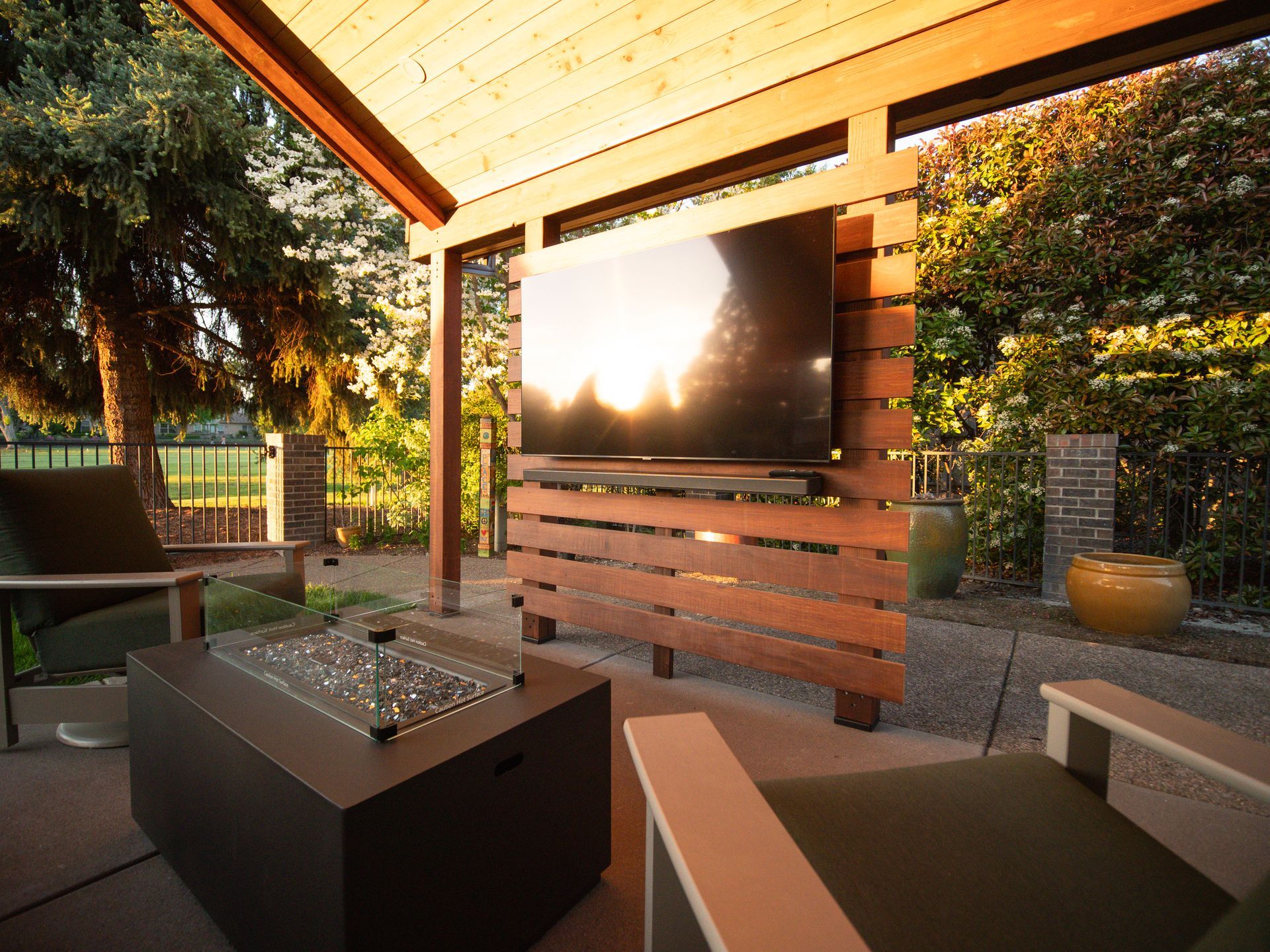 Outdoor patio with a mounted TV on a wooden screen, fire pit, and seating.