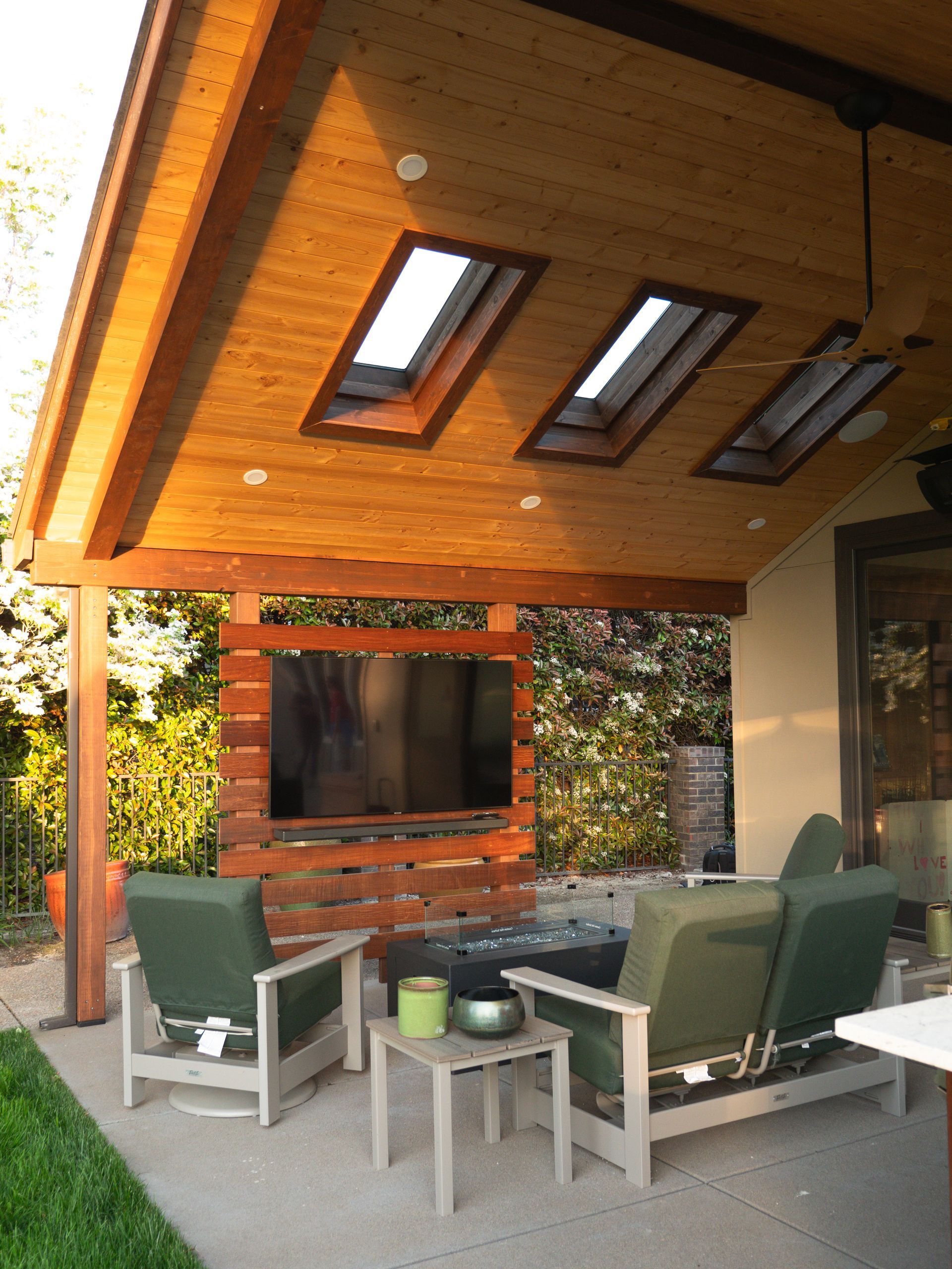 Outdoor patio with wood ceiling, skylights, furniture, large TV, and green chairs.