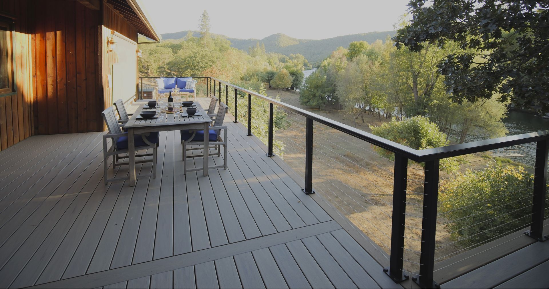 Wooden deck with dining table overlooking a river and trees.
