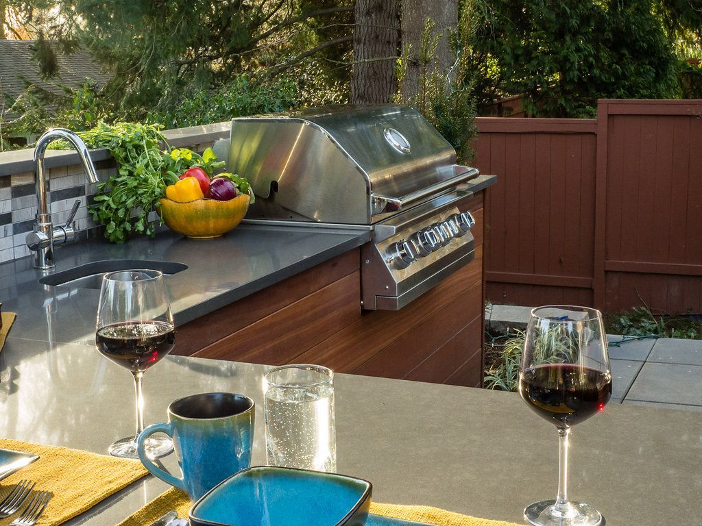 Outdoor kitchen with grill, sink, countertop, glasses of wine, and colorful fruit bowl.