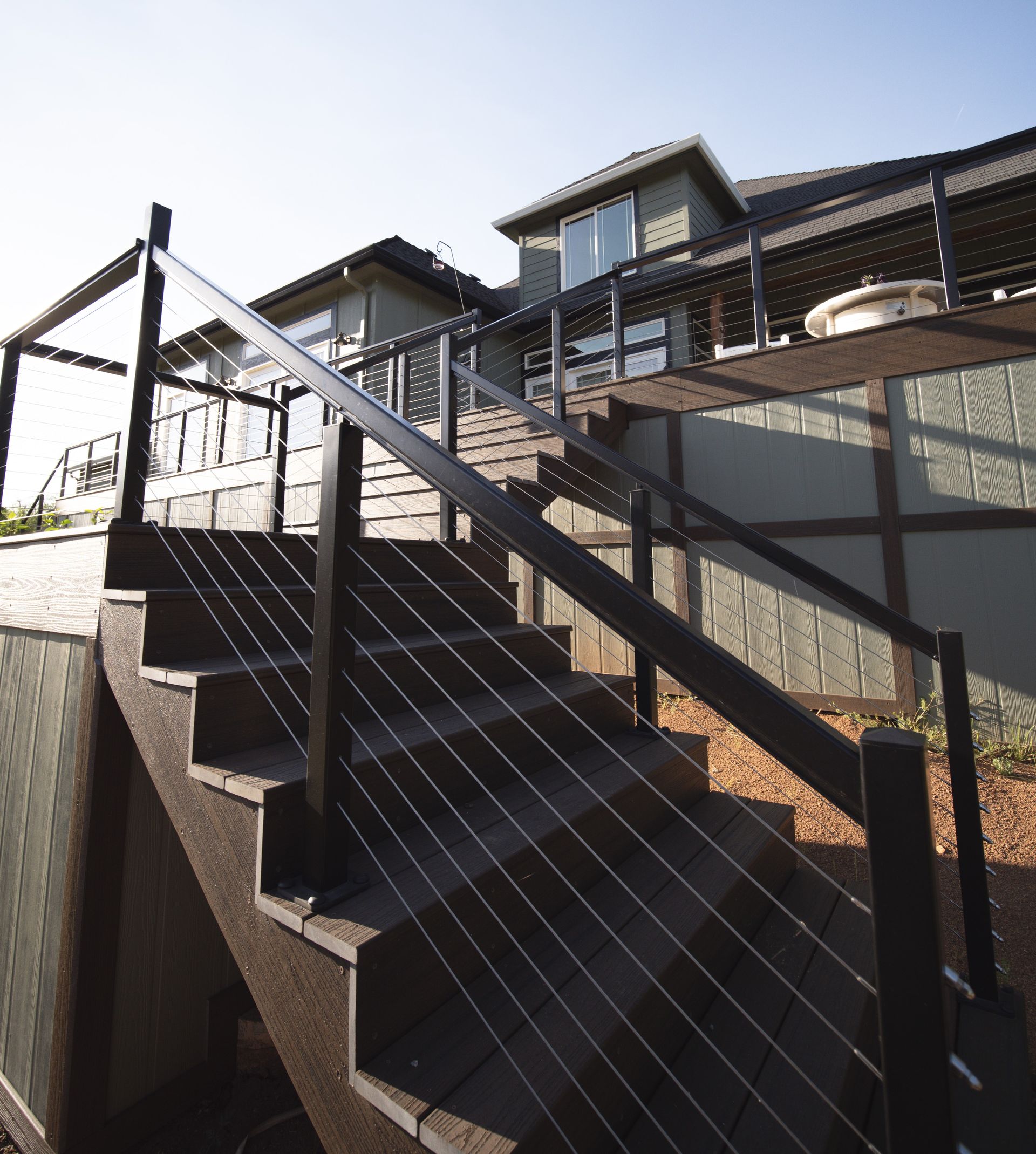 Dark brown staircase with cable railing leading up to a green house with deck.