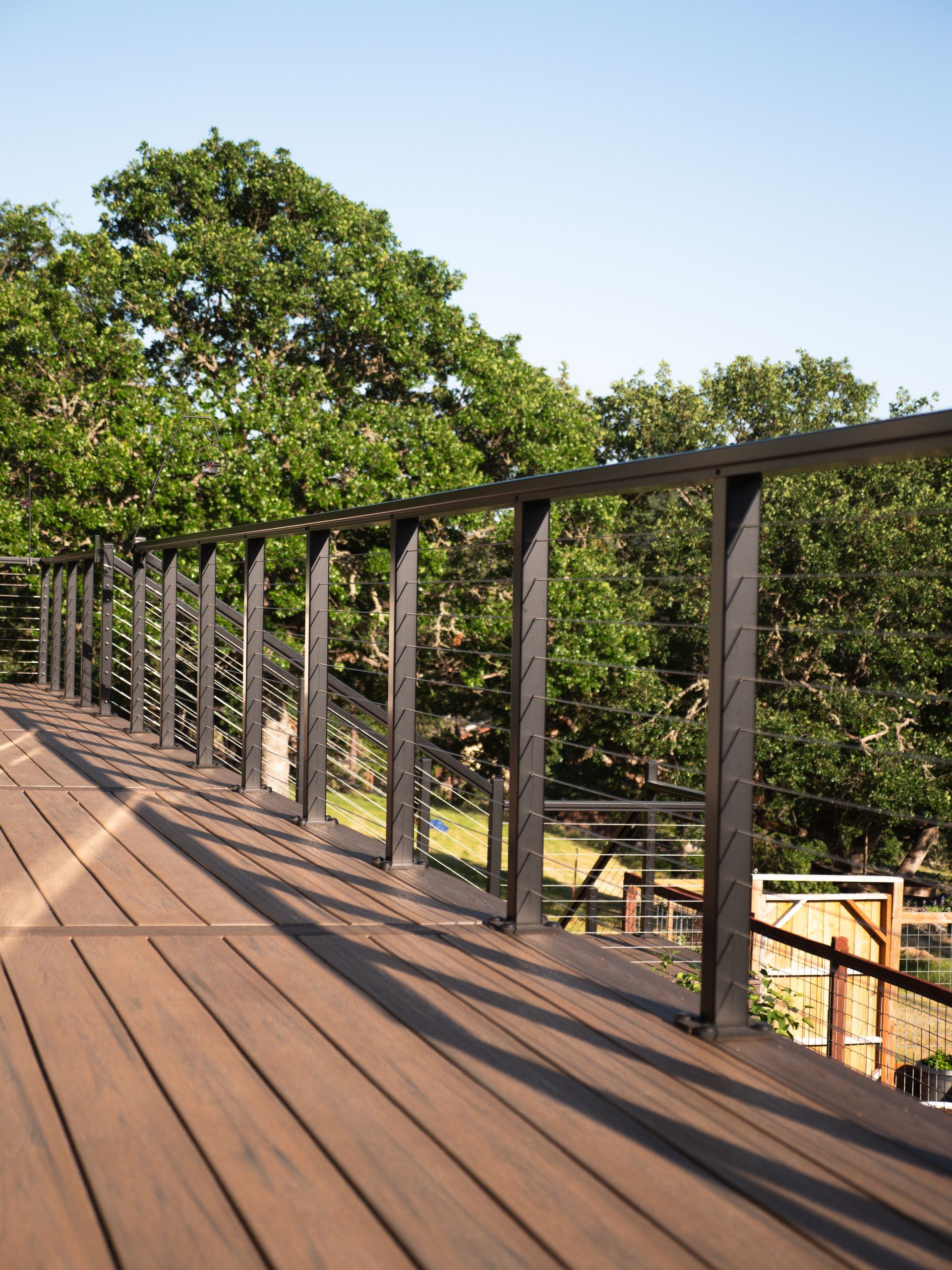 Brown wooden deck with dark metal railing, trees in background, blue sky.