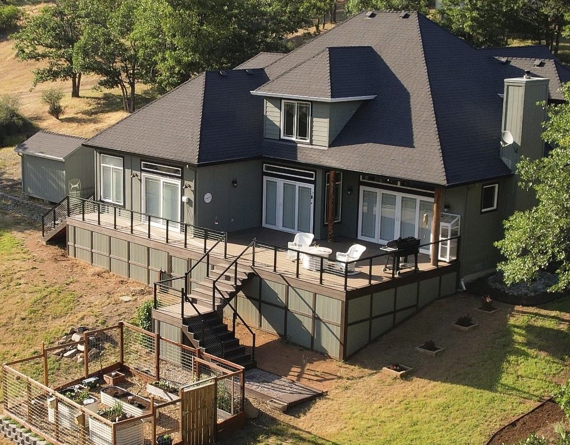 Green house with a large deck, overlooking a garden, set in a sunny, grassy area.