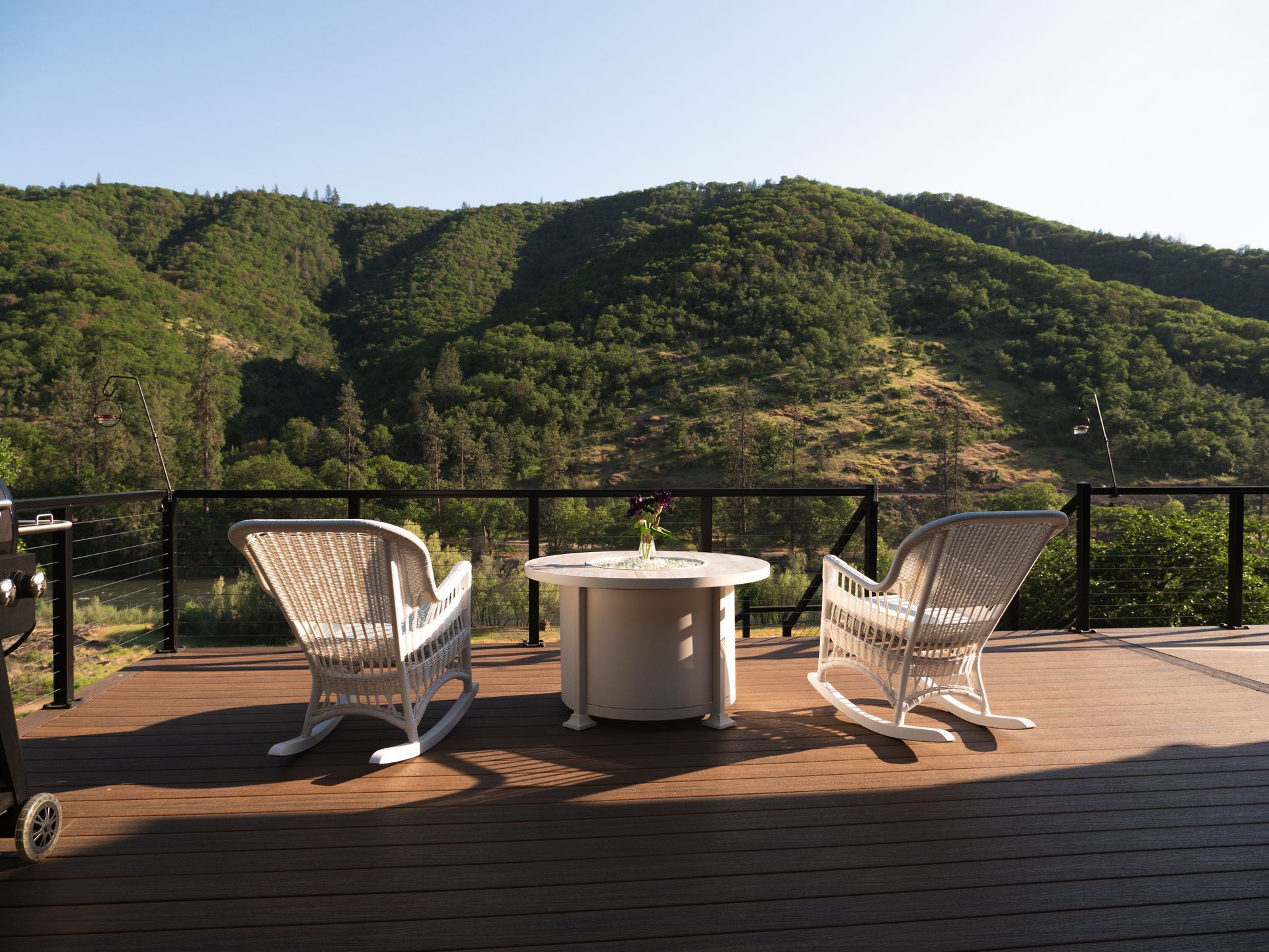 Two white rocking chairs face a small table with a mountain backdrop.