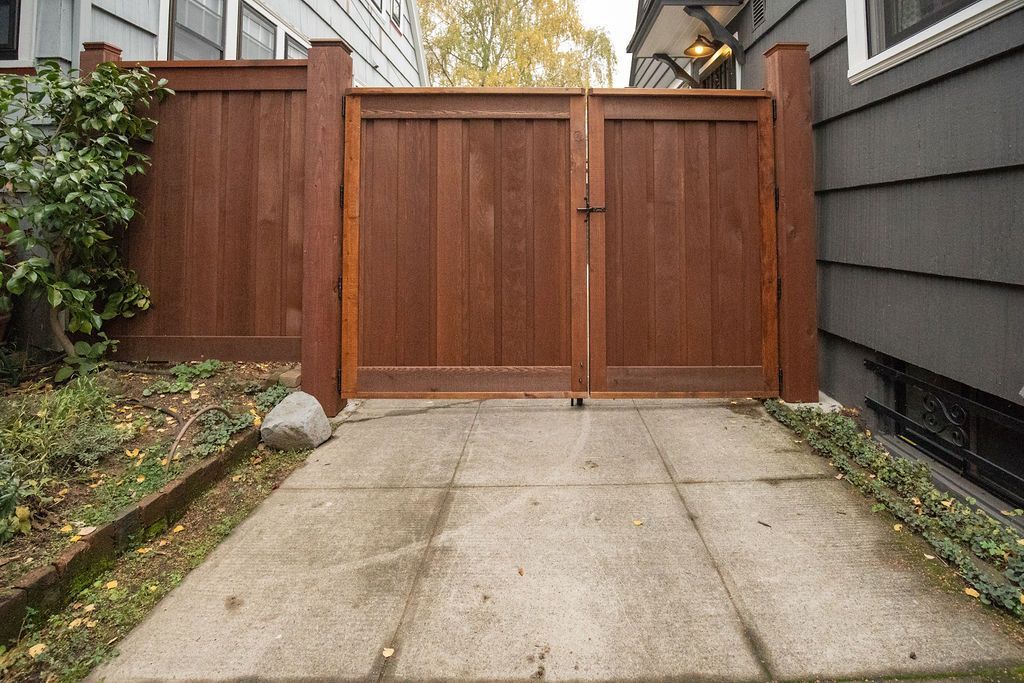 A wooden fence surrounds a concrete driveway in front of a house.