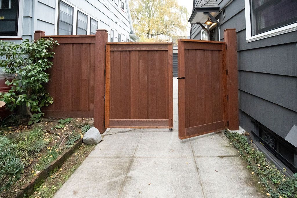 A wooden gate is open to a driveway leading to a house