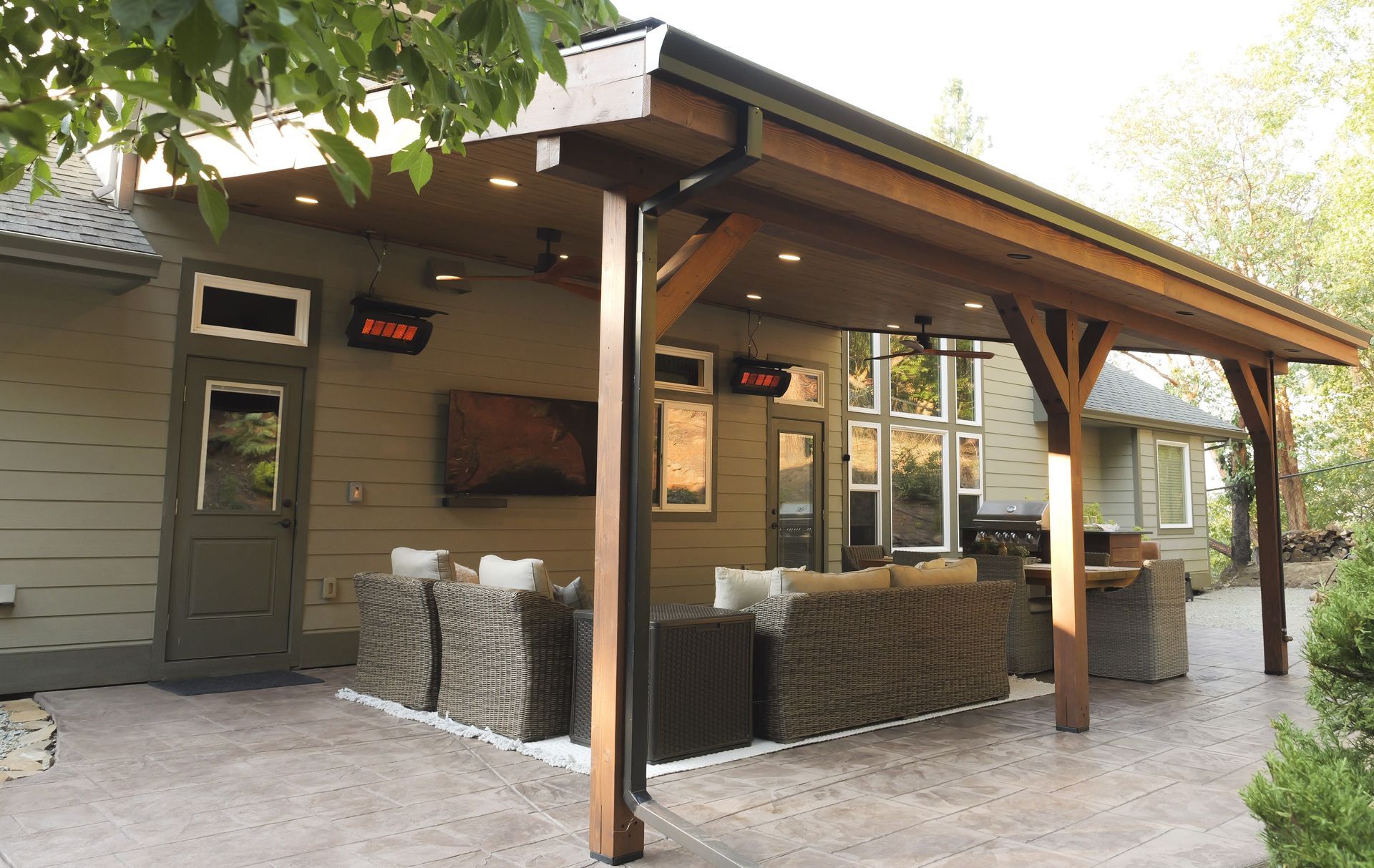 Outdoor patio with seating under a wooden canopy, featuring heaters and a TV.