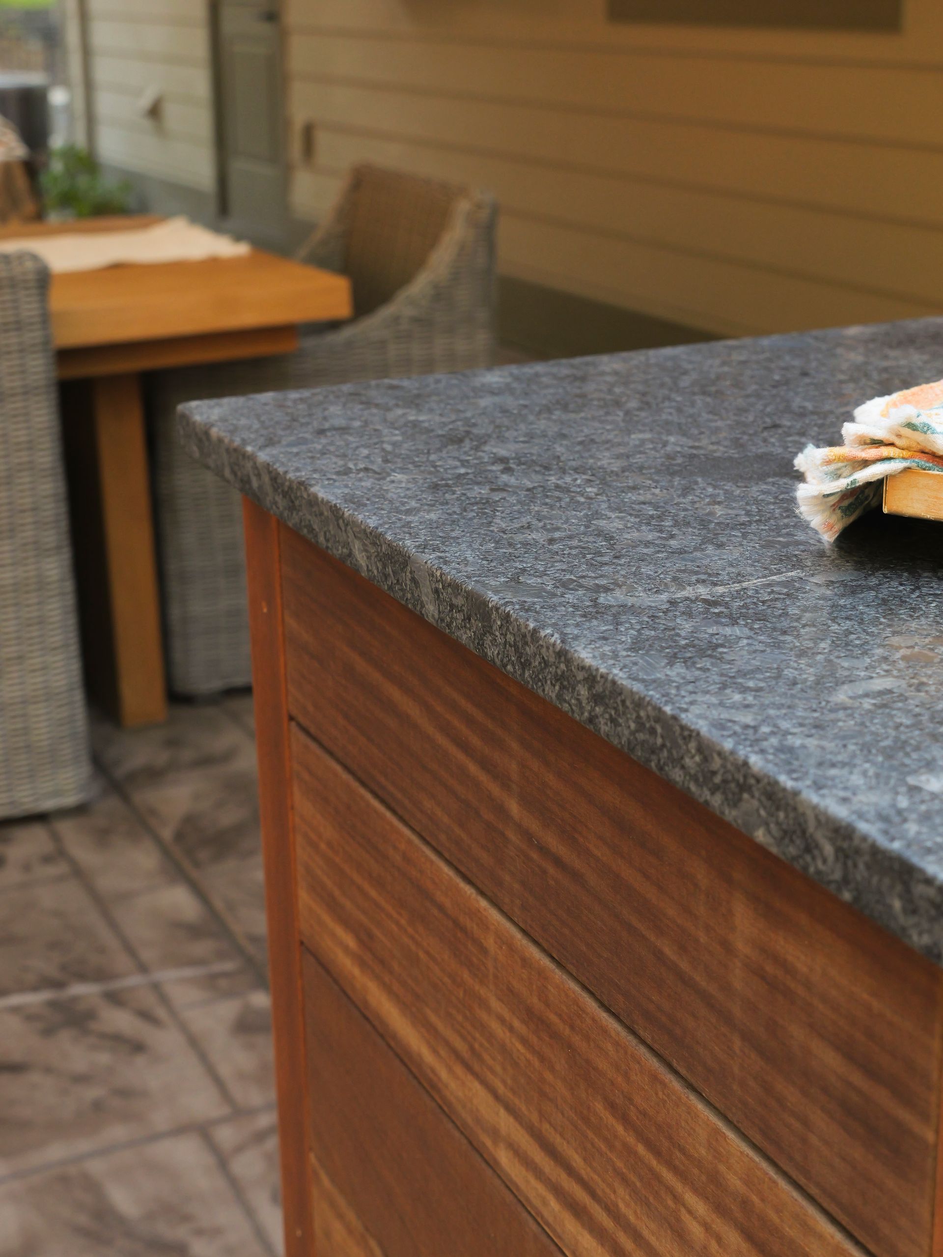 Outdoor kitchen with granite countertop and wooden cabinetry; patio setting.