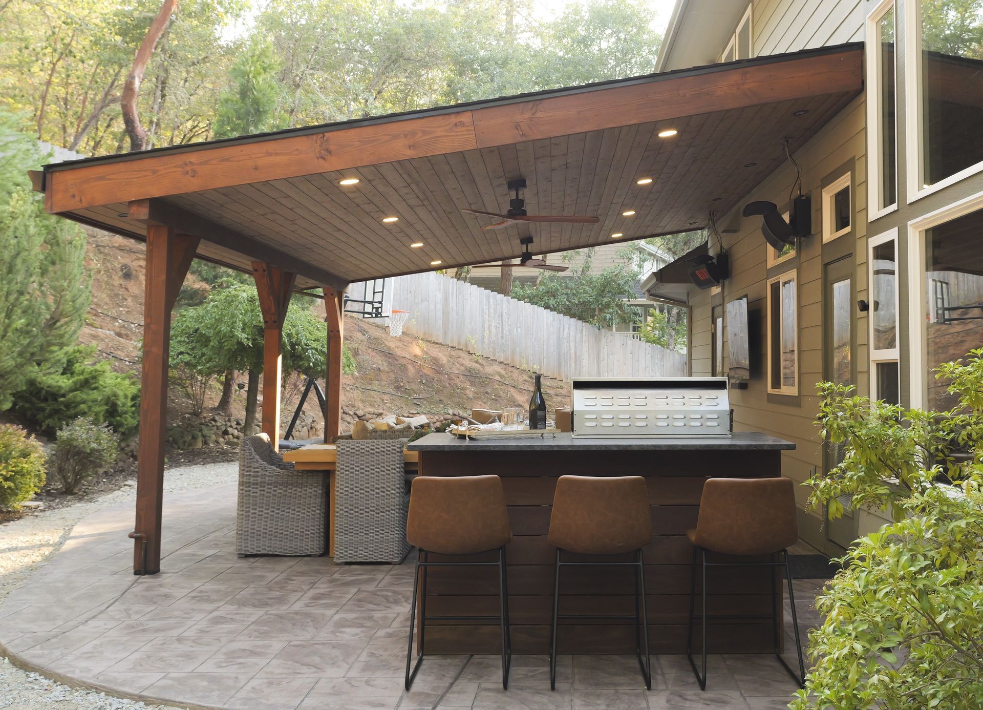 Patio with bar, seating, and built-in grill under a wooden awning.