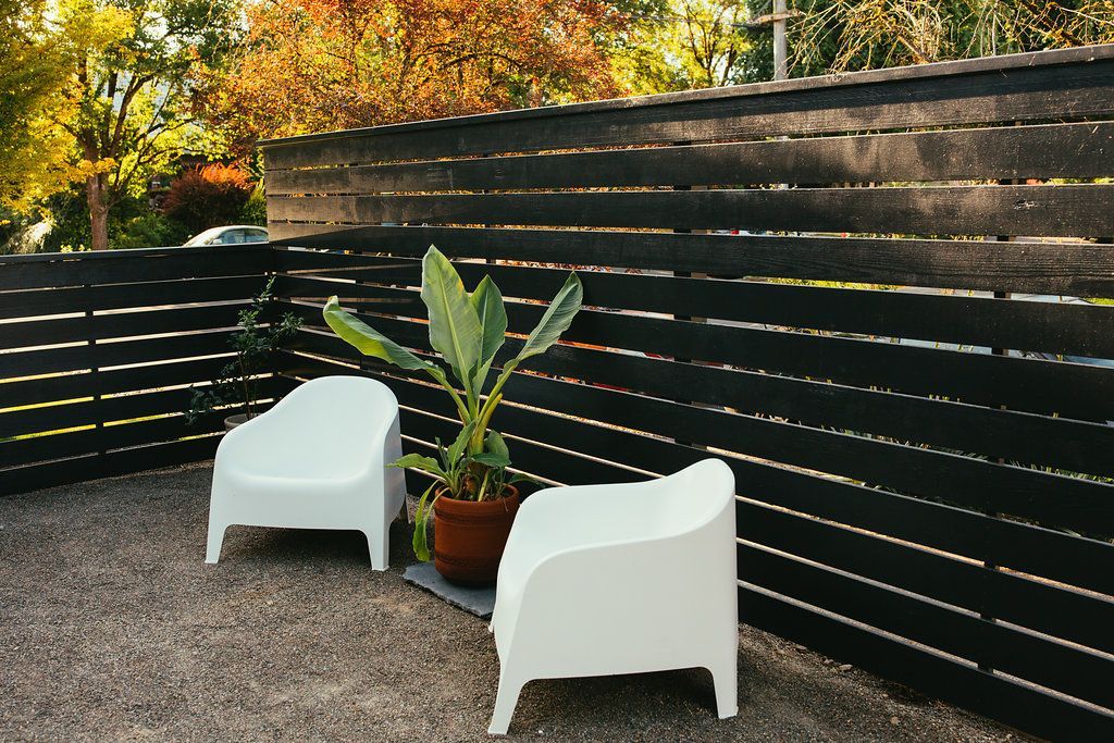 Two white chairs and a potted plant are sitting in front of a wooden fence.