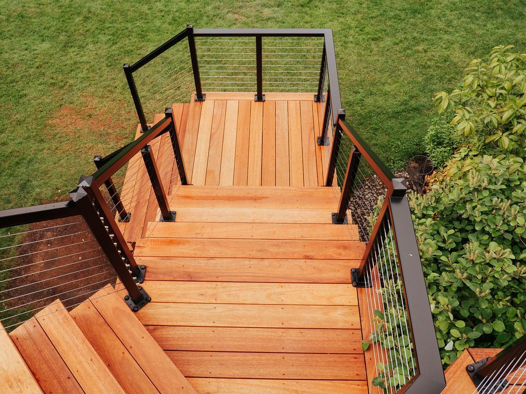 Wooden outdoor staircase with black railings and a grassy background.