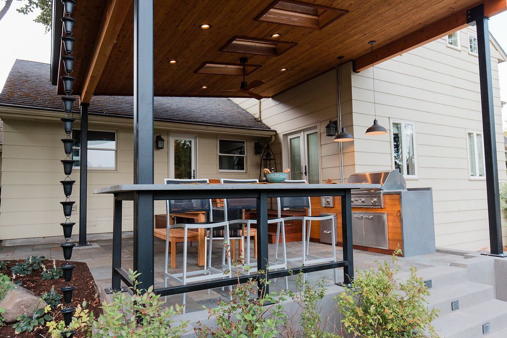 Outdoor kitchen with a bar, overhead cover, and stainless steel appliances.