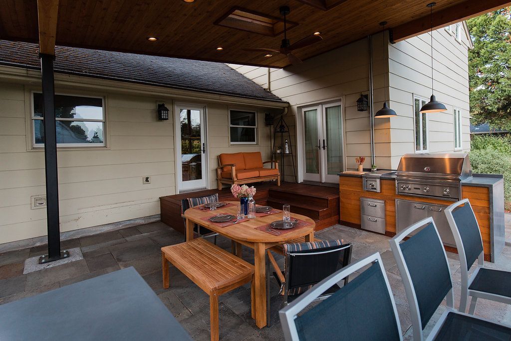 Outdoor patio with dining area, grill, and seating under a wooden roof; neutral tones.