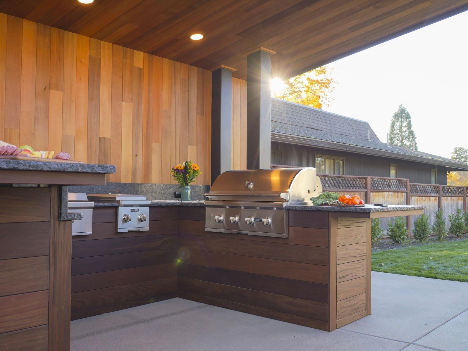 Outdoor kitchen with a stainless steel grill, wooden cabinetry, and a concrete patio.
