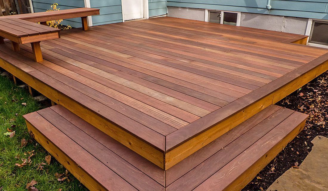 A wooden deck with stairs and a bench in front of a house.