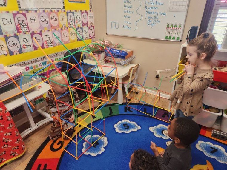 A group of children are playing with straws in a classroom.