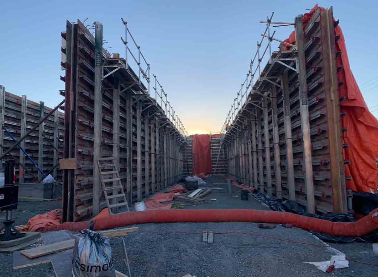 Ouvrier du bâtiment sur une échelle, travaillant sur un coffrage de mur en bois à l'intérieur d'un grand bâtiment.