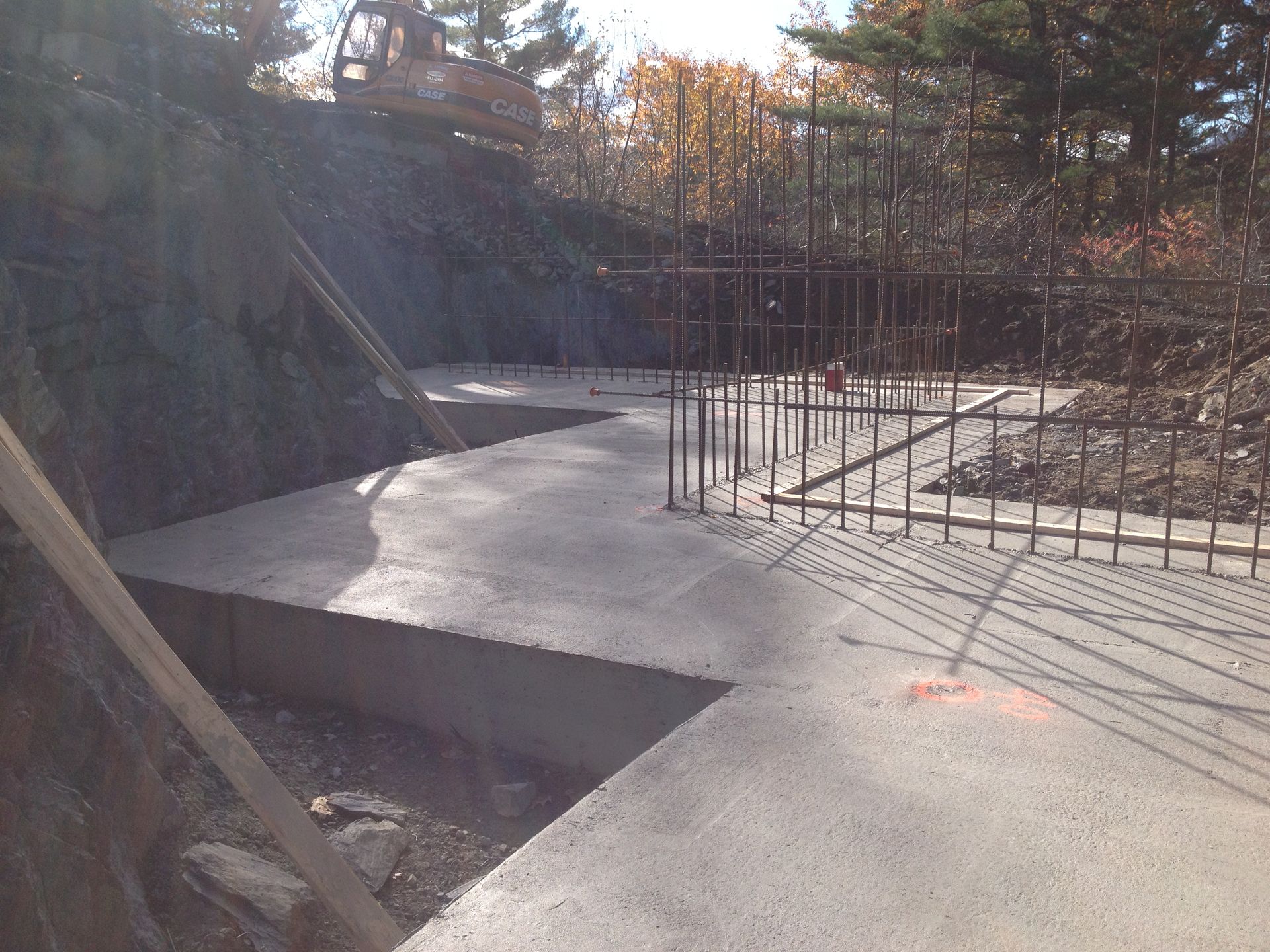 Chantier de construction avec fondation en béton fraîchement coulée et ossature en ferraillage.