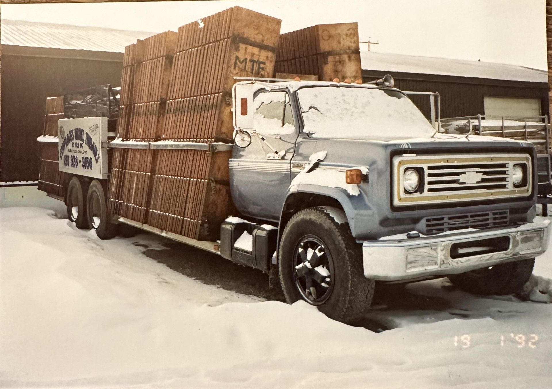 Un camion Chevy bleu chargé de caisses en bois est assis dans la neige, daté de 19 '92.
