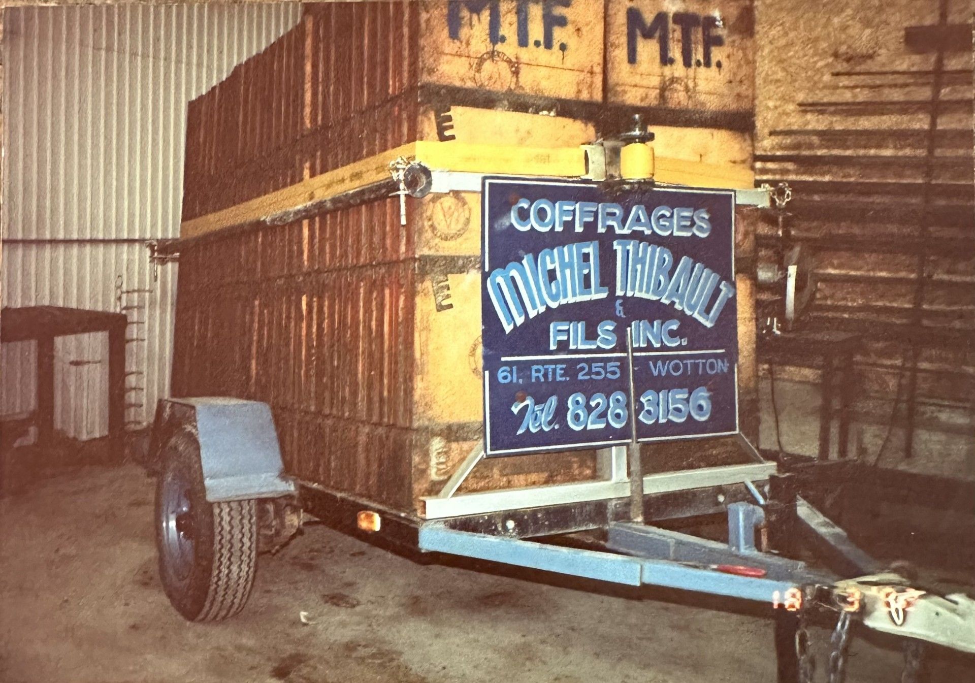 Une remorque chargée de caisses en bois étiquetées « COFFRAGES MICHEL THIBAULT », transportant probablement des matériaux de construction.