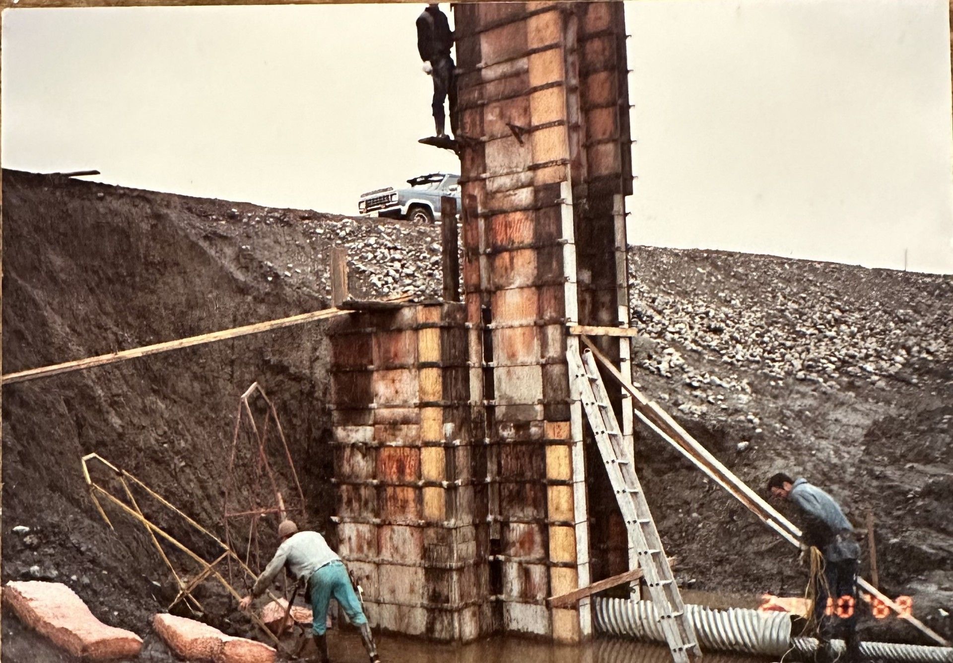 Des ouvriers du bâtiment construisent une structure en béton dans un environnement extérieur boueux.