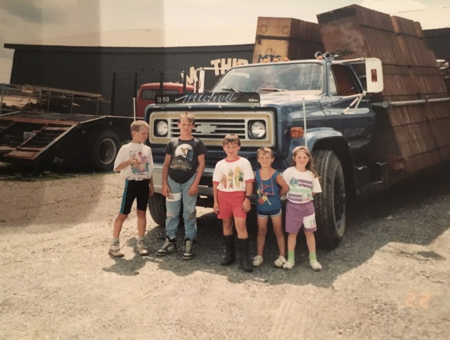 Des enfants se tiennent devant un grand camion bleu aux parois latérales en bois. Le camion est garé devant un bâtiment.