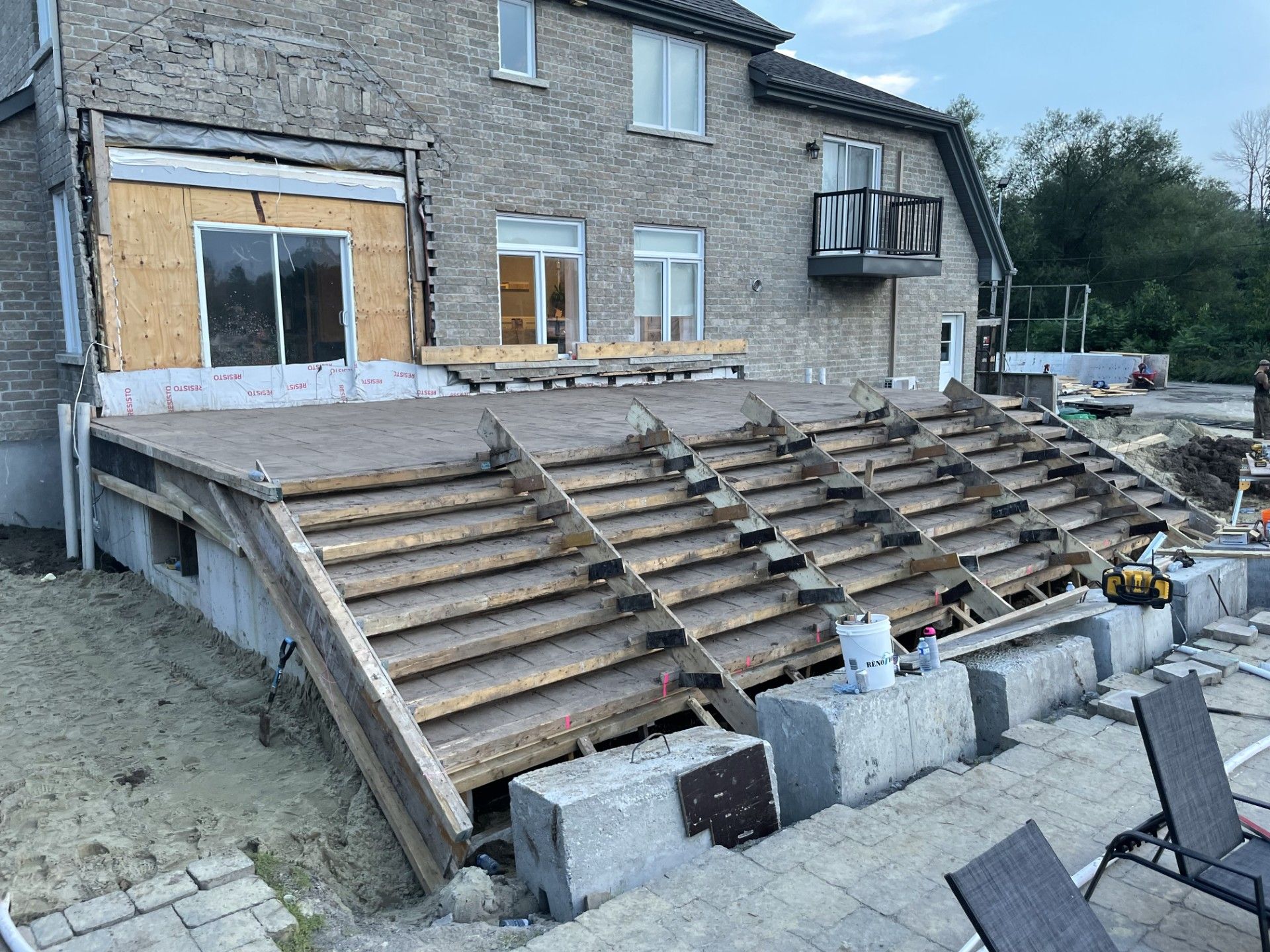 Cour arrière en construction : terrasse avec escalier menant à un patio en pierre près d'une maison en brique.