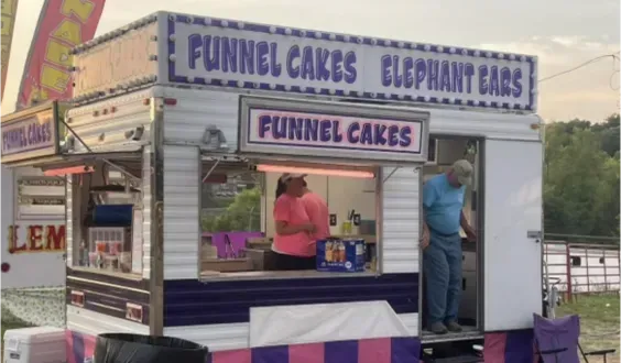 Funnel cake and elephant ear food stand with workers serving customers outdoors