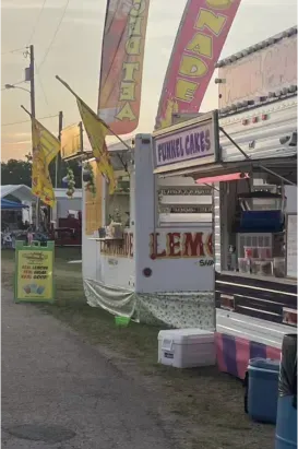 Fairground food stalls with colorful vertical signs and a lemonade stand along a walkway
