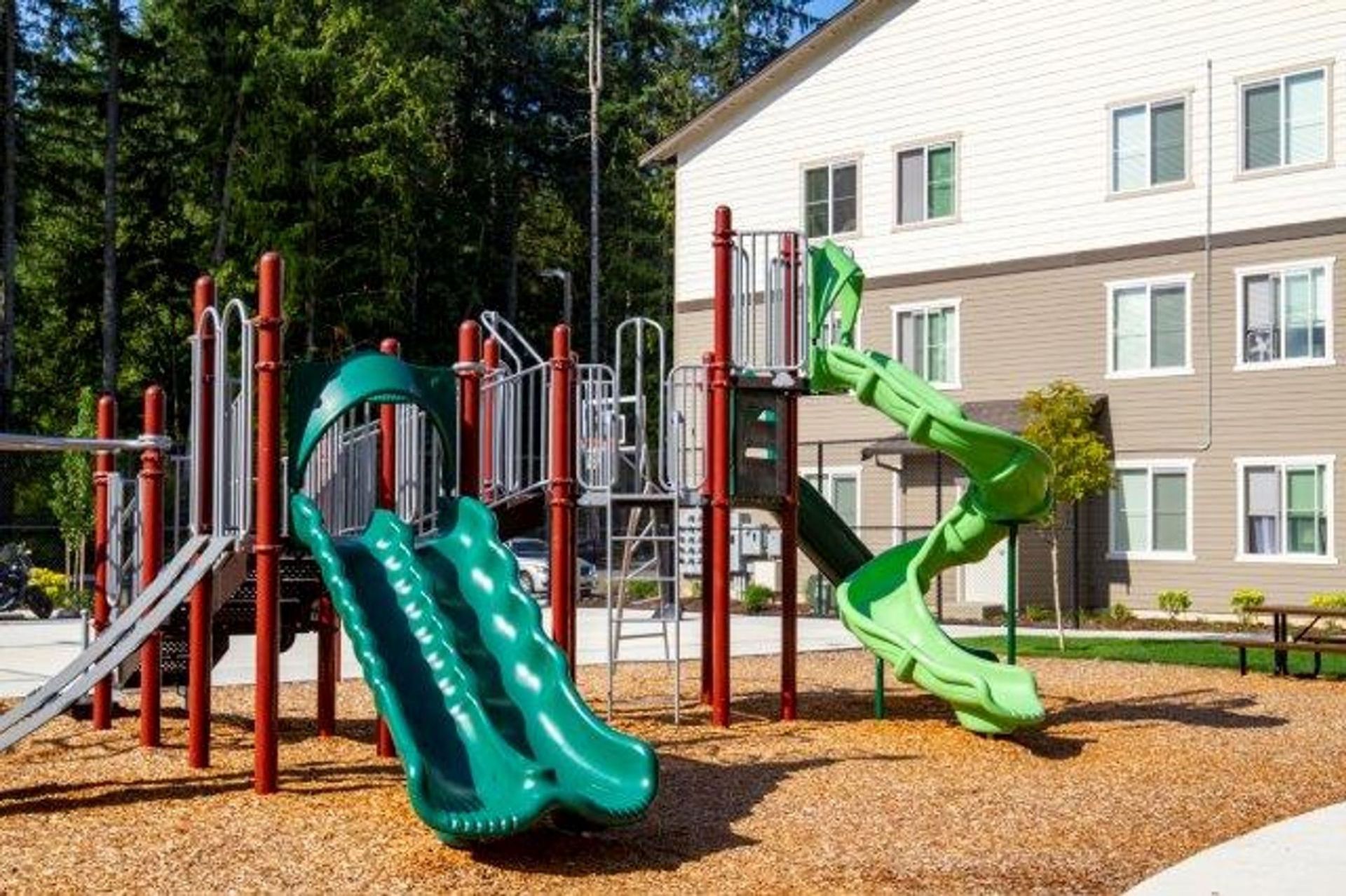 A playground with a green slide and a red slide in front of a building.