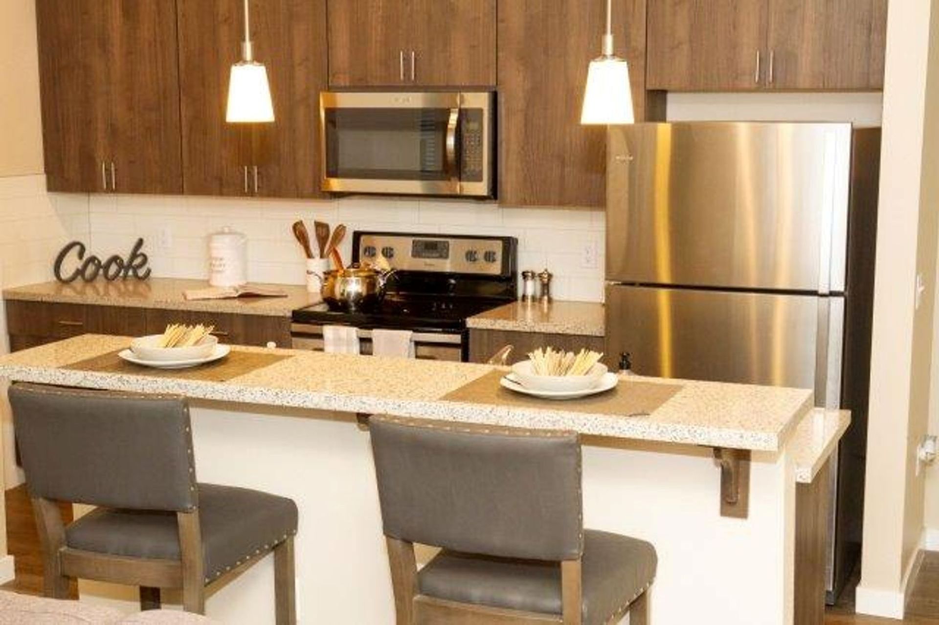 A kitchen with a stainless steel refrigerator , stove , microwave and two chairs.