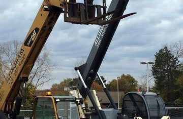 Yellow And Black Telehandler With Extended Forks.